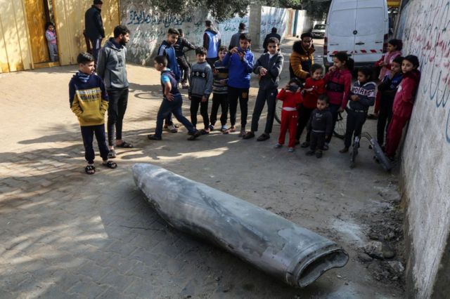 فلسطینی‌ها در کنار یک بمب منفجر نشده ایستاده‌اند که جنگنده اف-۱۶ اسرائیل در دیرالبالح در مرکز نوار غزه پرتاب کرده بود